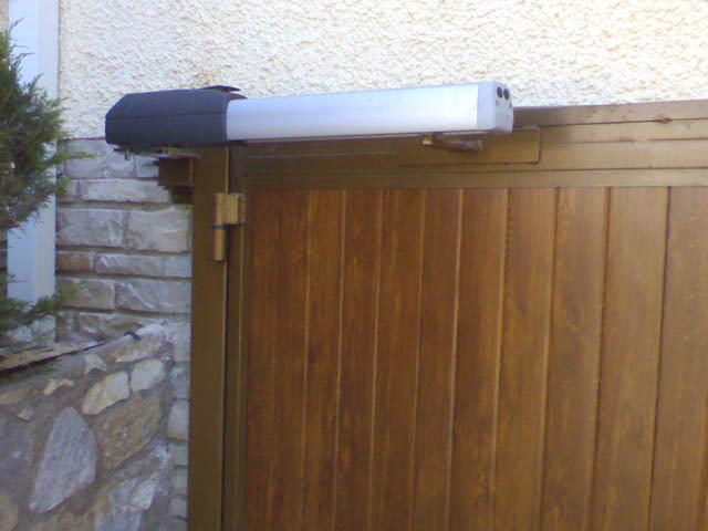 Puerta batiente, con panel sandwich imitación madera y automatismo en parte superior