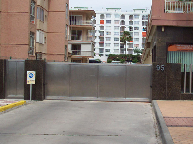 Puerta corredera de acero inoxidable, con puerta peatonal de igual terminación